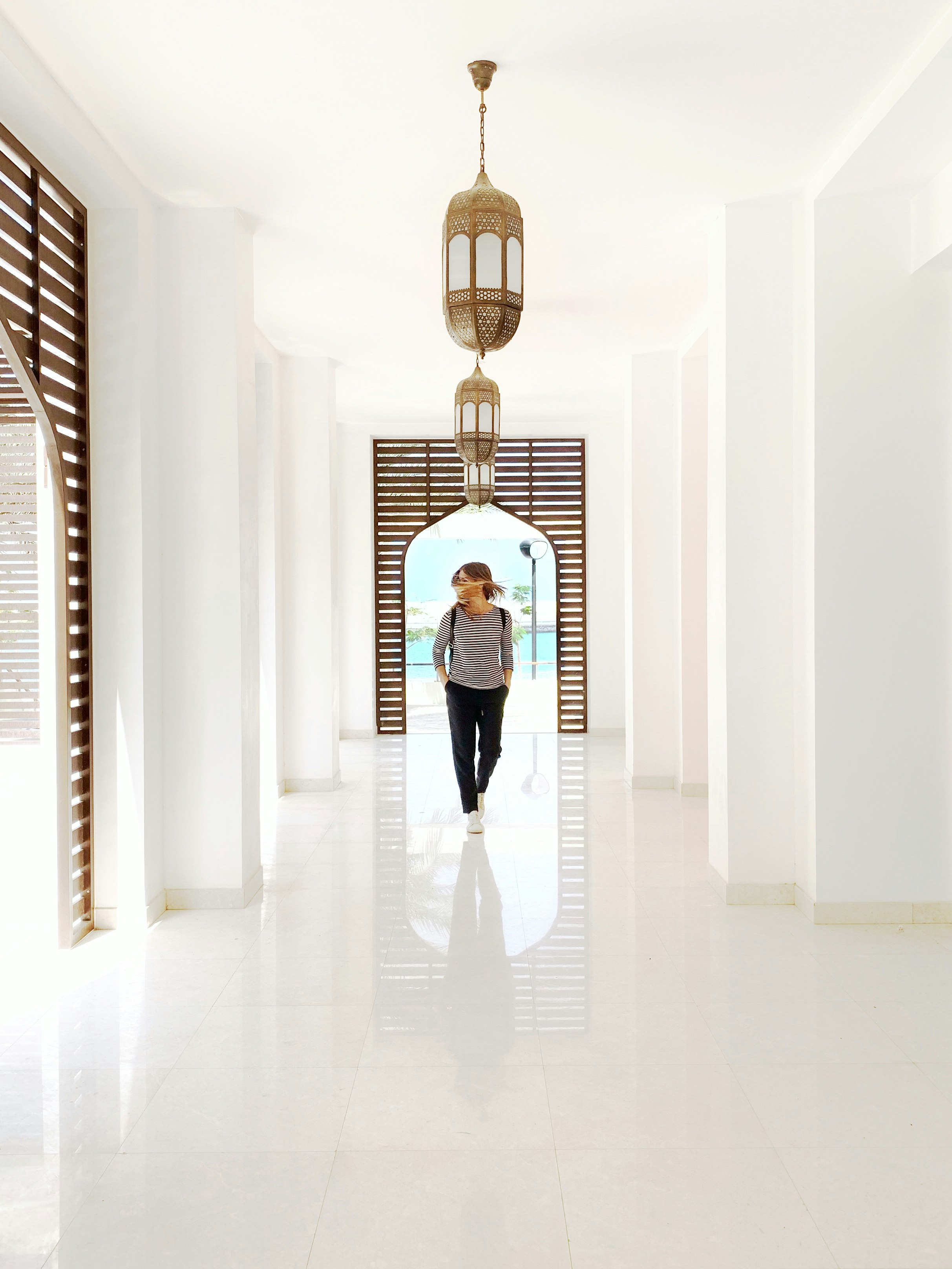 person wearing black pants standing below gold pendant lamp